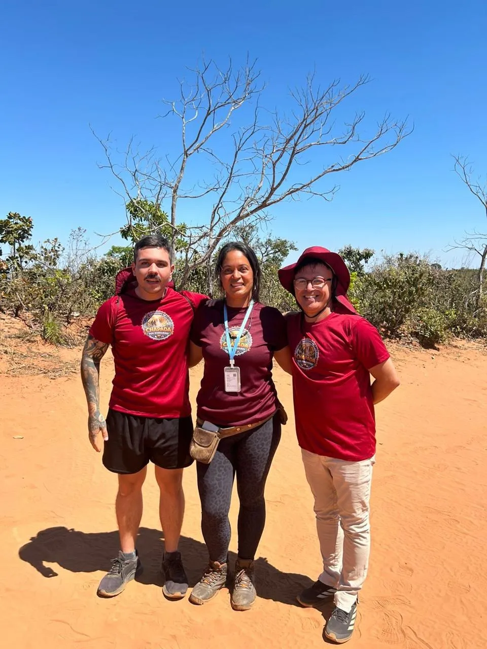 Equipe do Turistando: três integrantes de camiseta vinho com a logo do projeto, em trilha no cerrado